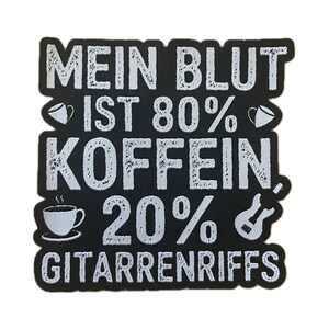 May include: Black patch with white text: "MEIN BLUT IST 80% KOFFEIN 20% GITARRENRIFFS." Includes coffee cup and guitar graphics. The patch is rectangular with rounded corners.