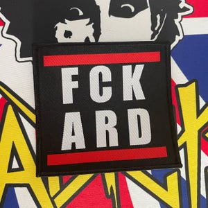 May include: Black and red embroidered patch with the text "FCK ARD" in white.