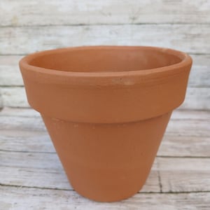 May include: A terracotta flower pot with a rounded bottom and a wide opening. The pot is made of unglazed clay and has a natural brown color.