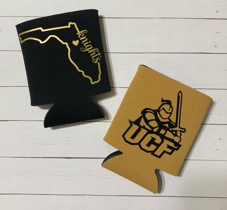 Op de afbeelding: Twee zwarte en gouden blikjeskoelers. Een koeler heeft een zwarte omtrek van de staat Florida met een hart en het woord "knights". De andere koeler heeft een zwarte ridder die een zwaard vasthoudt met de letters "UCF" in zwart.