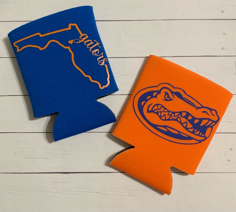 Op de afbeelding: Twee schuimrubberen blikjeskoelers. E&eacute;n is blauw met een oranje omtrek van de staat Florida en de tekst "gators". De andere is oranje met een blauwe alligator-kopgrafiek.