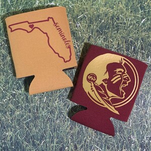 Op de afbeelding: Twee schuimrubberen blikjeskoelers, een is beige met een rode omtrek van de staat Florida en het woord "Seminoles" erop gedrukt, de andere is bordeauxrood met een gouden omtrek van een Indiaans hoofd met een veer en de letters "FSU" erop gedrukt.