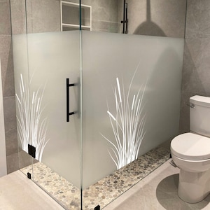 May include: A modern glass shower enclosure with a frosted glass panel featuring a white reed design. The shower has a black handle and hinges, a pebble stone base, and a black shower head.