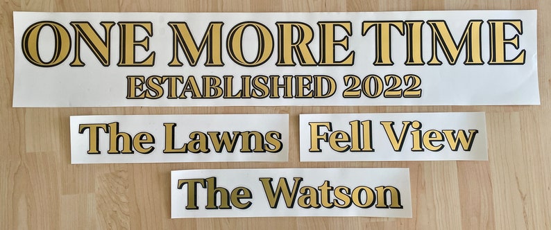 May include: Several white rectangular decals with gold lettering and black outlines. The largest decal reads "ONE MORE TIME ESTABLISHED 2022." Smaller decals say "The Lawns," "Fell View," and "The Watson."