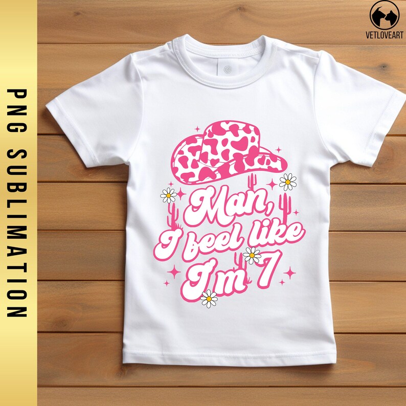 May include: White t-shirt with a pink cowgirl hat, cacti, and the text "Man, I feel like I'm 7".