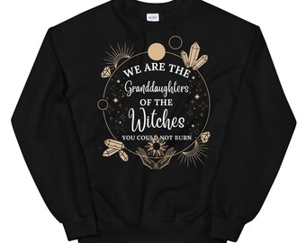 Może przedstawiać: Czarna bluza z nadrukiem w kolorze złotym, na którym widnieje napis "We are the Granddaughters of the Witches You could not burn". Nadruk zawiera okrąg ze gwiazdami, księżycami i kryształami.