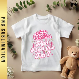 May include: White t-shirt with a pink cowgirl hat, cacti, and the text "Man, I feel like I'm 7".