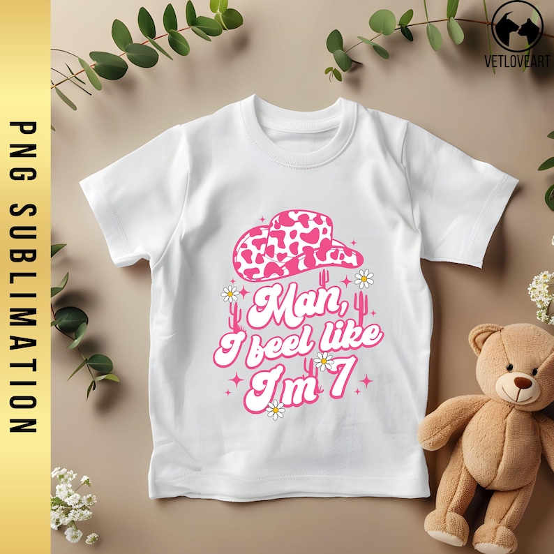May include: White t-shirt with a pink cowgirl hat, cacti, and the text "Man, I feel like I'm 7".