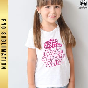 May include: A white t-shirt with a pink graphic design of a cowboy hat, cacti, and the text "Man, I feel like I'm 7".