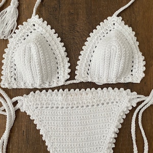 May include: White crochet bikini top and bottom with a scalloped edge. The top has a triangle shape and the bottom is a high-waisted style.