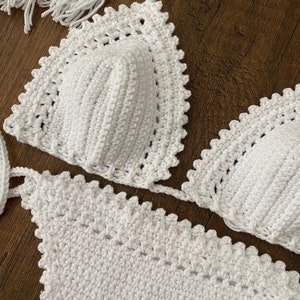 May include: White crochet bikini top and bottom with a scalloped edge. The top has a triangle shape and the bottom is a simple, high-waisted style.