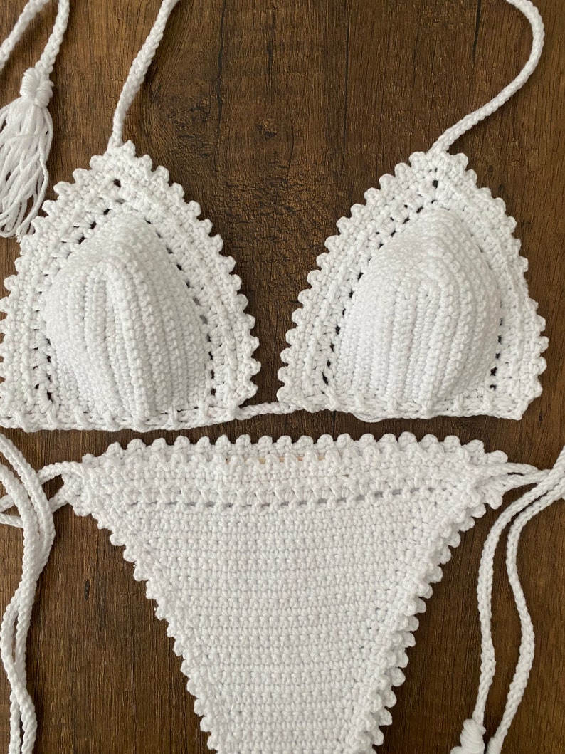 May include: White crochet bikini top and bottom with a scalloped edge. The top has a tie closure at the neck and back. The bottom has a tie closure on the sides.