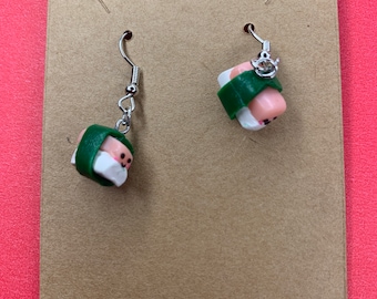 Può includere: Un paio di orecchini pendenti a forma di rotoli di sushi in miniatura realizzati in argilla bianca e rosa, avvolti da una fascia verde scuro. Ogni pezzo di sushi presenta un piccolo viso sorridente dipinto a mano e un gancio in metallo argentato.
