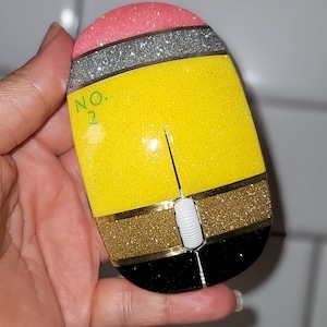 Könnte beinhalten: Eine gelbe, rosa, goldene, silberne und schwarze Glitzermaus in Form eines Bleistifts. Die Maus hat ein weißes Scrollrad und der Text "NO. 2" ist an der Seite geschrieben.