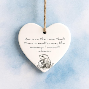 May include: A white heart-shaped ceramic ornament suspended by a jute string. It features a black and white illustration of a bear and a small animal, with the text "You are the love that time cannot erase, the memory I cannot release."
