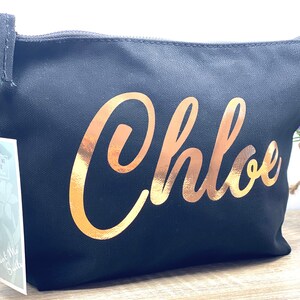 Peut inclure: Pochette de maquillage en toile noire avec le nom "Chloe" imprimé en or sur le devant.