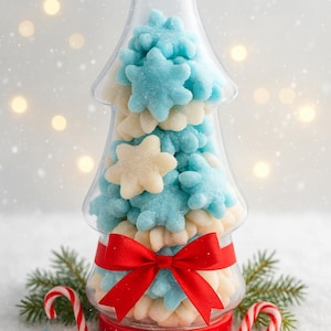 Puede incluir: Un recipiente transparente en forma de árbol lleno de caramelos con forma de copo de nieve azules y blancos. El recipiente está atado con una cinta roja. Bastones de caramelo y copos de nieve decorativos están esparcidos en la base.