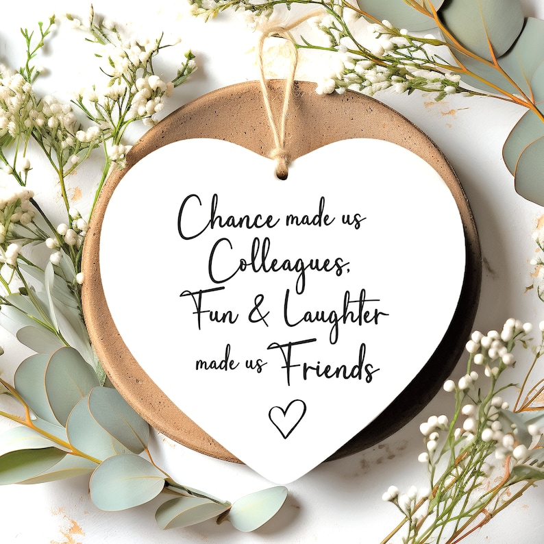 Op de afbeelding: Witte hartvormige plaquette met de tekst "Chance made us Colleagues. Fun & Laughter made us Friends" in zwarte cursieve letters. Een klein hartje is onderaan de tekst getekend.