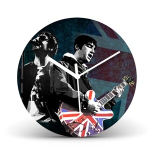 May include: A round clock with a black background and a Union Jack design. The clock features a black and white image of two musicians, one playing a guitar with a Union Jack design. The clock hands are white.