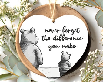 Può includere: Ciondolo in ceramica bianco a forma di cuore con un'illustrazione in bianco e nero di Winnie the Pooh e Maialino. Il ciondolo ha il testo "never forget the difference you make" stampato su di esso.