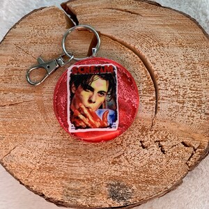 May include: Red round keyring with a silver key ring. The keyring features a picture of a man with a red background and the word "SCREAM" in white letters.