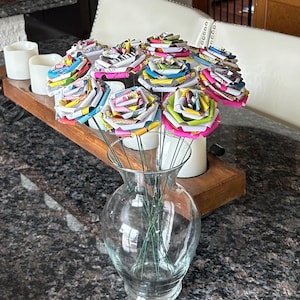Puede incluir: Un ramo de rosas de papel de colores en un jarrón de vidrio transparente. Las rosas están hechas de papel reciclado y tienen una variedad de patrones y colores, incluyendo rosa, azul, verde y amarillo.