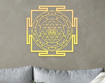 May include: A gold-colored metal wall decor featuring a geometric design with a mandala-like pattern. The design is a square with a circle in the center, and the circle is filled with a series of triangles and lines.