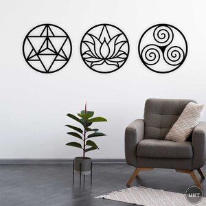 May include: Three black metal wall decor pieces in the shape of circles. The circles feature geometric designs, including a lotus flower, a triskelion, and a geometric star. The decor is displayed on a white wall with a gray armchair and a potted plant in the foreground.