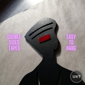 May include: Black silhouette of a person with a red rectangle on the head. The text "DOUBLE SIDED TAPES" is on the left and "EASY TO HANG" is on the right. The text "UNT" is in the bottom right corner.