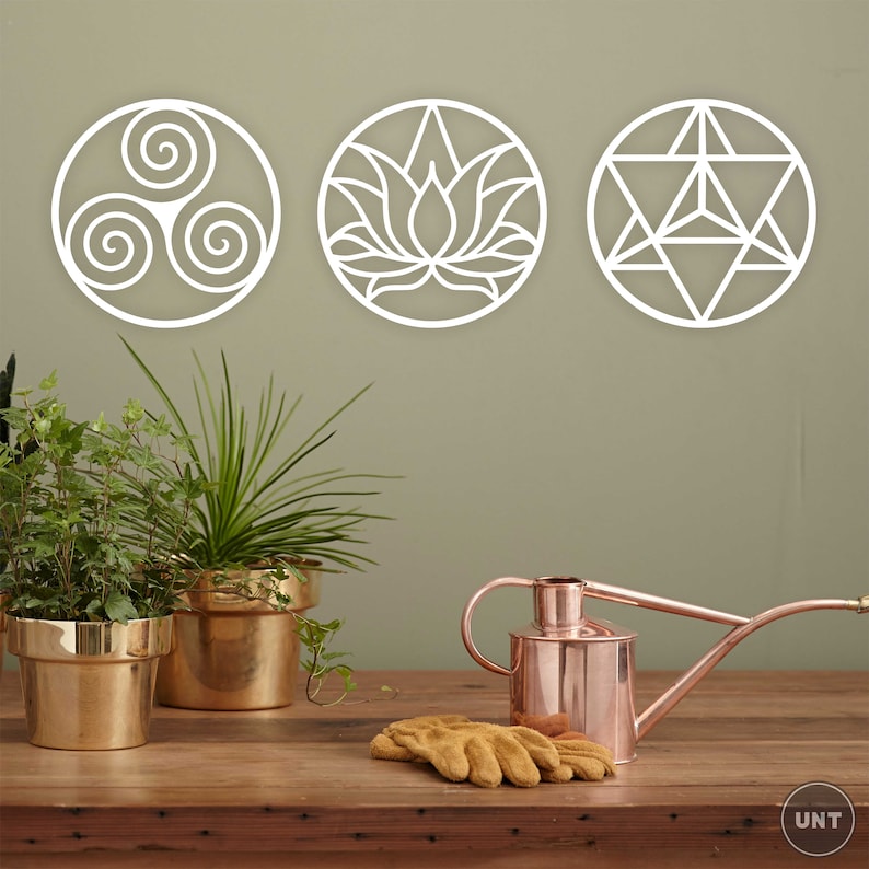 May include: Three white metal wall decor pieces with geometric designs. The designs include a triple spiral, a lotus flower, and a star of David. The pieces are hanging on a light green wall.