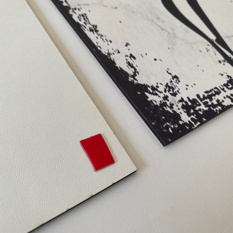 May include: Two white surfaces with black edges. One surface has a red square sticker on it. The other surface has a black and white abstract design.