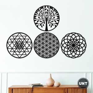 May include: Four black circular wall art pieces. One features a tree design, another a geometric pattern, a third a flower-like design, and the last a Sri Yantra symbol. The art is displayed on a white wall above a wooden cabinet.