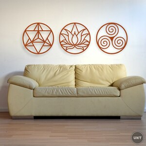 May include: Three circular wall decor pieces with intricate designs. The first piece features a geometric pattern, the second a lotus flower, and the third a triple spiral. The pieces are all made of a dark brown material and are mounted on a white wall above a beige couch.
