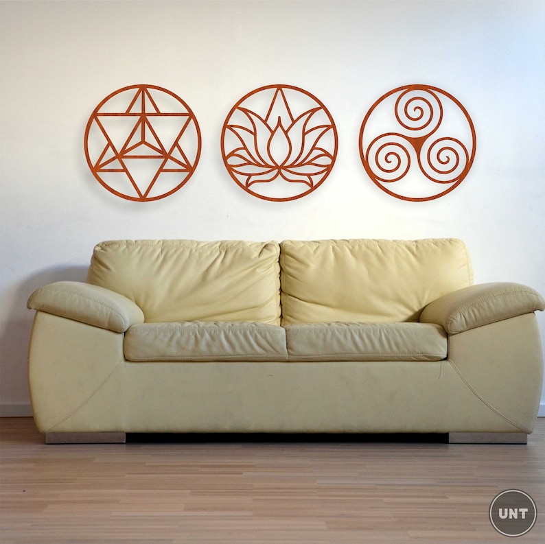 May include: Three circular wall decor pieces with intricate designs. The first piece features a geometric pattern, the second a lotus flower, and the third a triple spiral. The pieces are all made of a dark brown material and are mounted on a white wall above a beige couch.