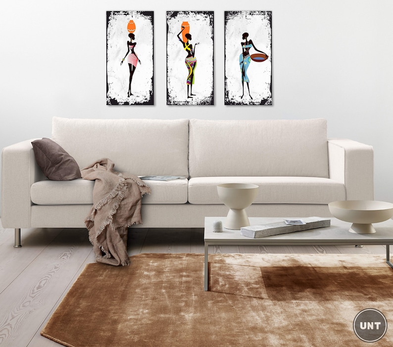 May include: Three framed art prints featuring stylized black figures of women in colorful clothing. The prints are hung on a white wall above a white couch.