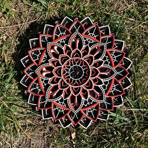May include: A black and white mandala with red accents. The mandala is made of wood and has a layered design. It is a decorative piece that can be used to add a touch of bohemian style to any room.
