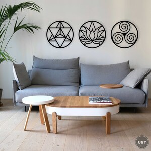 May include: A gray sofa with three black wall decorations featuring geometric designs. The sofa is in a living room with a white coffee table and a smaller white side table. The coffee table has a book on it.