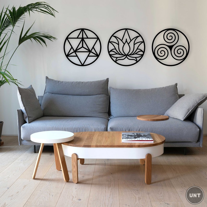 May include: A gray sofa with three black wall decorations featuring geometric designs. The sofa is in a living room with a white coffee table and a smaller white side table. The coffee table has a book on it.