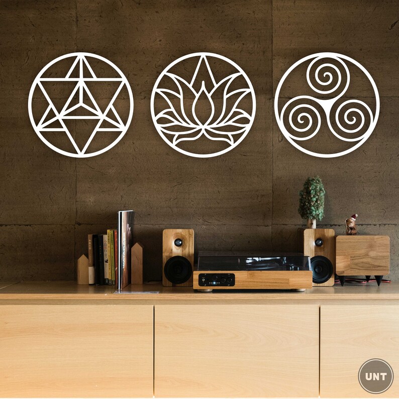 May include: Three white metal wall decor pieces with geometric designs. The first piece is a star with a triangle inside. The second piece is a lotus flower. The third piece is a triple spiral. The pieces are hanging on a brown wall.