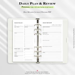 Peut inclure: Un agenda blanc avec un classeur argenté, ouvert sur une page de planification et de révision quotidienne. Le texte "DAILY PLAN & REVIEW" est en haut, avec "PERSONAL (95 x 171 mm / 3.74 x 6.37 INCH)" en dessous. L'agenda comprend des sections pour les objectifs, l'emploi du temps et la réflexion.