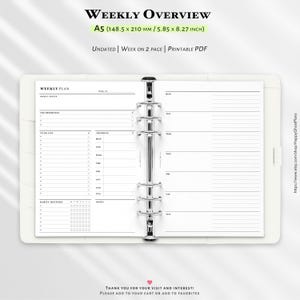 May include: A white A5 planner with a weekly overview layout. The planner includes sections for goals, to-do lists, spending, and notes. The text "WEEKLY OVERVIEW" and "A5 (14.85 x 21 cm)" are visible. The planner is undated and designed for a week on two pages.