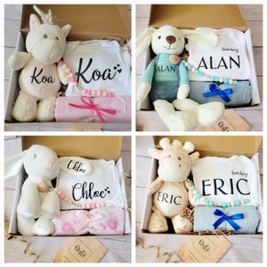 Könnte beinhalten: Vier Geschenkboxen mit personalisierten Babyartikeln. Jede Box enthält ein Plüschtier, einen Strampler, eine Decke und eine Holzperlenkette. Die Namen auf den Stramplern sind Koa, Alan, Chloe und Eric.