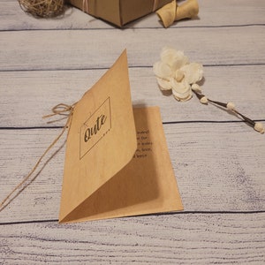 May include: A kraft paper card with the word "Cute" in a square frame, tied with twine. A brown gift box with pink and beige ribbon, a decorative ball, and a white flower are also visible.