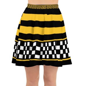 Puede incluir: Una falda skater con un diseño llamativo. Presenta rayas horizontales amarillas y negras, un patrón de cuadros y un patrón de greca dorada en la cintura. La falda se lleva con zapatos blancos.
