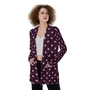 Könnte beinhalten: Ein langärmeliger Cardigan mit burgunderfarbenem Hintergrund und einem weißen Muster aus kleinen, stilisierten Figuren. Der Cardigan hat Taschen auf beiden Seiten und einen V-Ausschnitt.