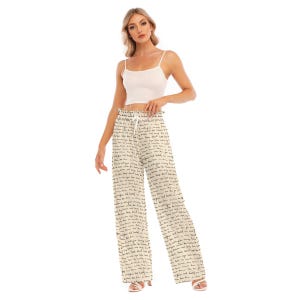 May include: White wide-leg trousers with a black print of the word "love" repeated all over. The trousers have a drawstring waist and are shown on a model wearing a white vest top.
