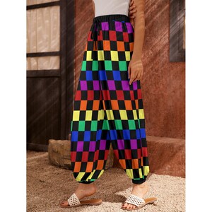 May include: Vibrant, chequered trousers with a drawstring waist and elasticated cuffs. The pattern displays squares of red, orange, yellow, green, blue, and purple on a black backdrop. The trousers are worn with white sandals.