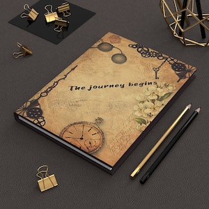 May include: A brown leather-bound journal with a vintage design featuring a pocket watch, a key, and a floral motif. The cover reads "The journey begins".