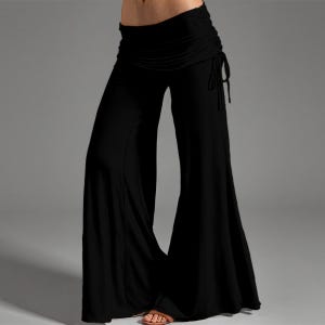 May include: Black palazzo pants with a wide leg design. The pants feature a ruched waistband with adjustable drawstring ties. The fabric appears to be a soft, flowing material, suitable for casual wear or yoga.