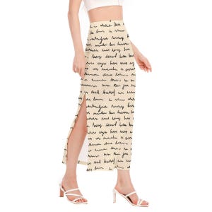 May include: A beige maxi skirt with a high waist and a side slit. The skirt is covered in a black handwritten script pattern.